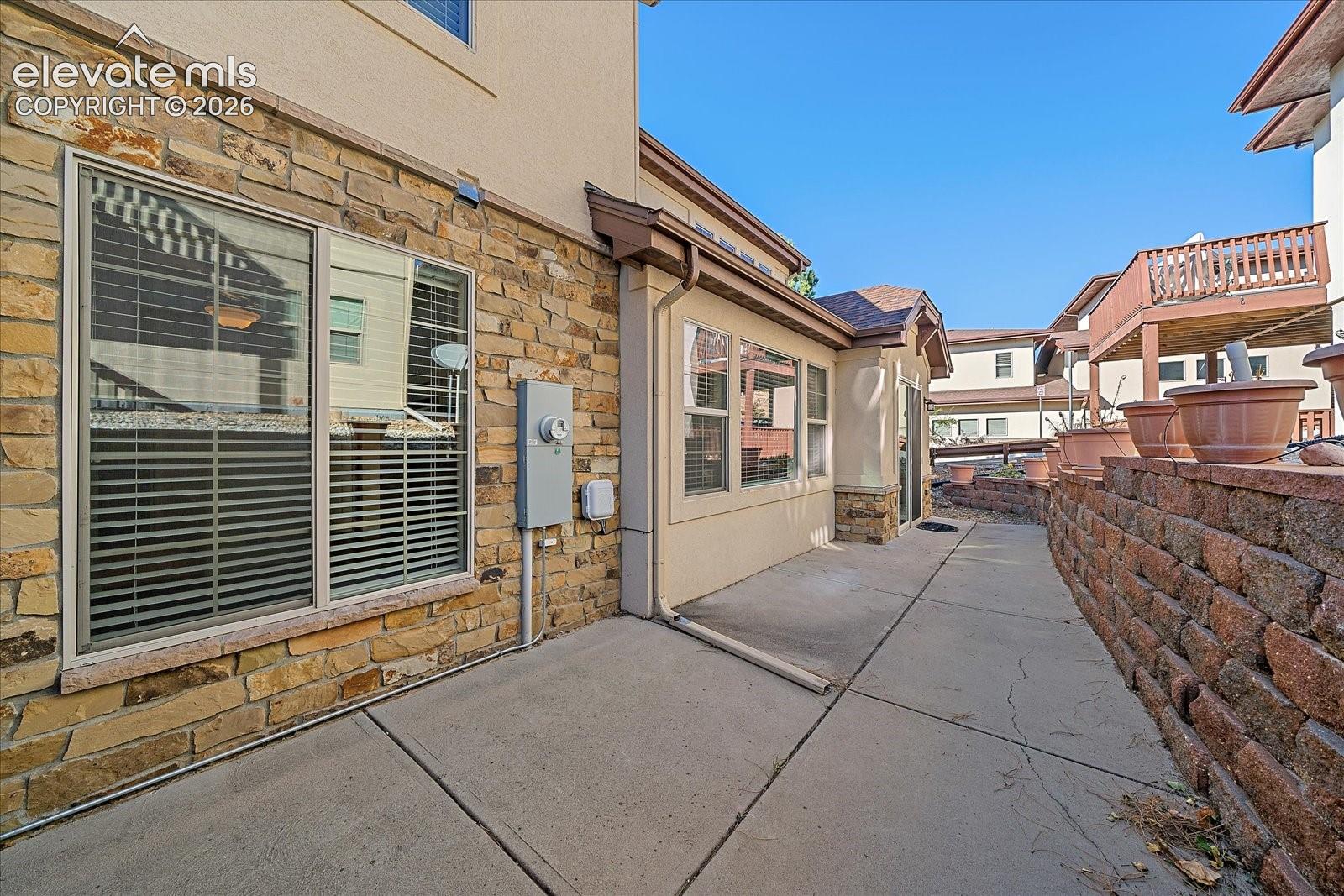 Exterior featuring stone veneer siding, concrete patio, and a tiered stone retaining wall