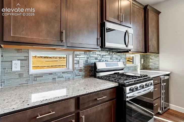 Dark wood-finish cabinetry, natural stone countertops, glass tile backsplash, stainless steel gas range, and built-in under-counter beverage chiller