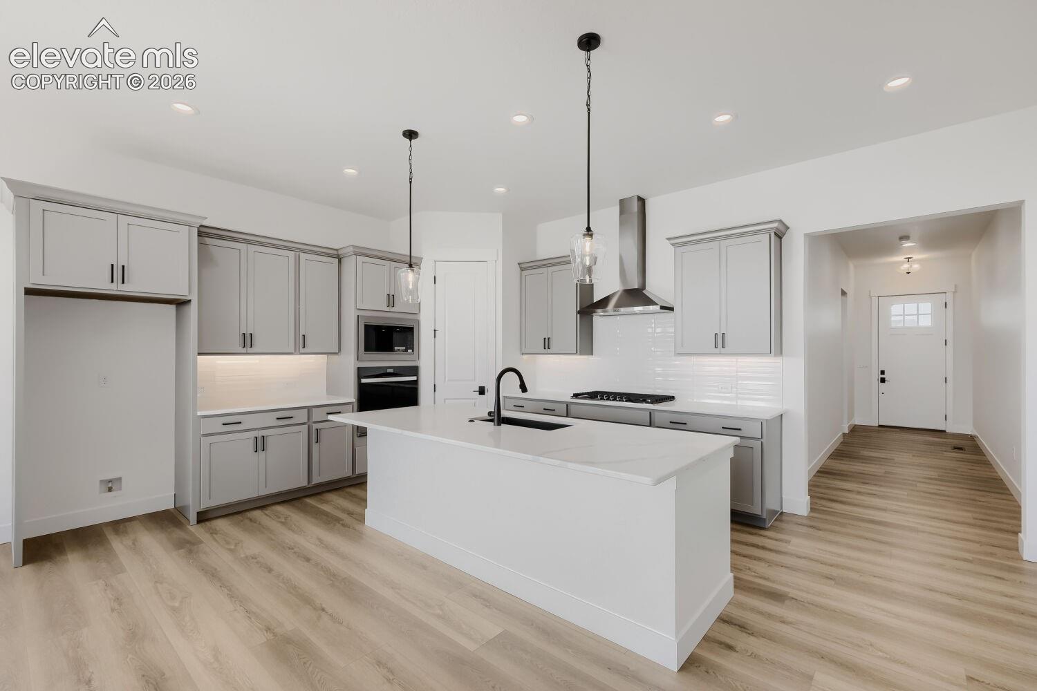 Modern kitchen featuring a central island, light wood-finish flooring, grey cabinetry, stainless steel appliances, and quartz countertops