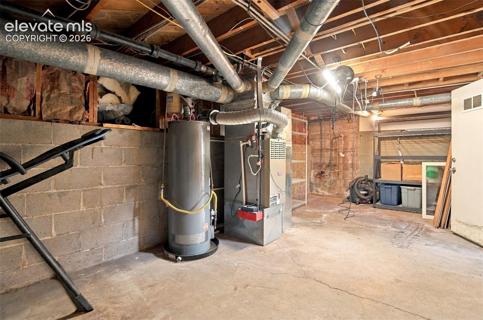 Unfinished basement featuring exposed floor joists, concrete block walls, a concrete floor, an integrated water heater, and a central heating unit