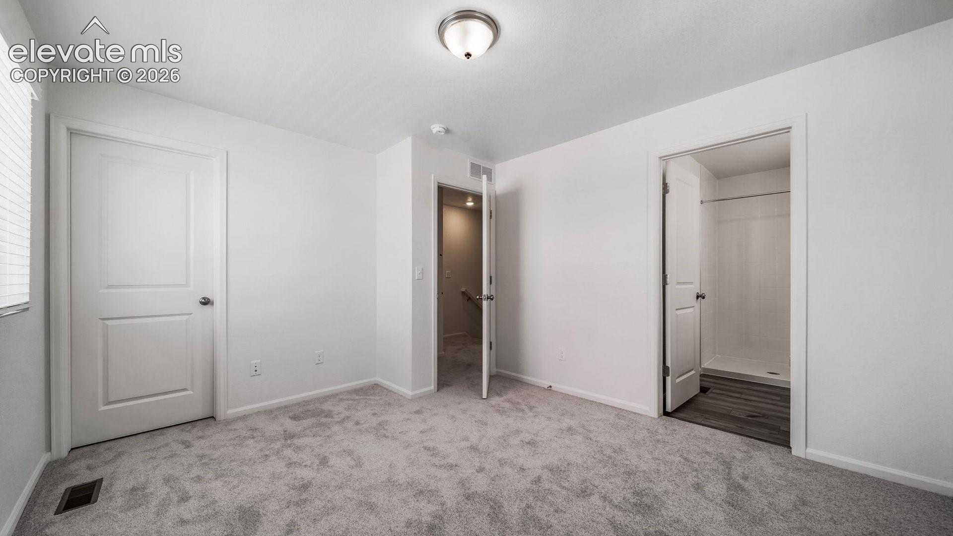 Room featuring neutral-toned carpeting, two-panel interior doors, and a central dome light fixture, with a doorway revealing a bathroom equipped with wood-finish flooring and a shower stall
*photos of a model home*
