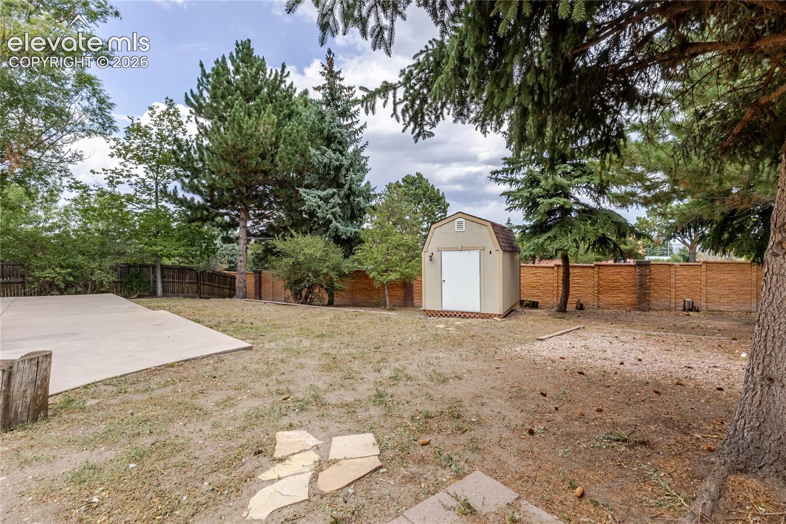 Expansive backyard featuring a concrete patio, mature trees, a storage shed, and a privacy fence