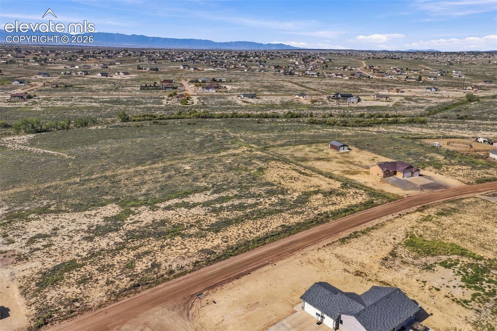 Expansive acreage featuring native high-desert terrain, a wide dirt road frontage, and prominent mountain range horizons