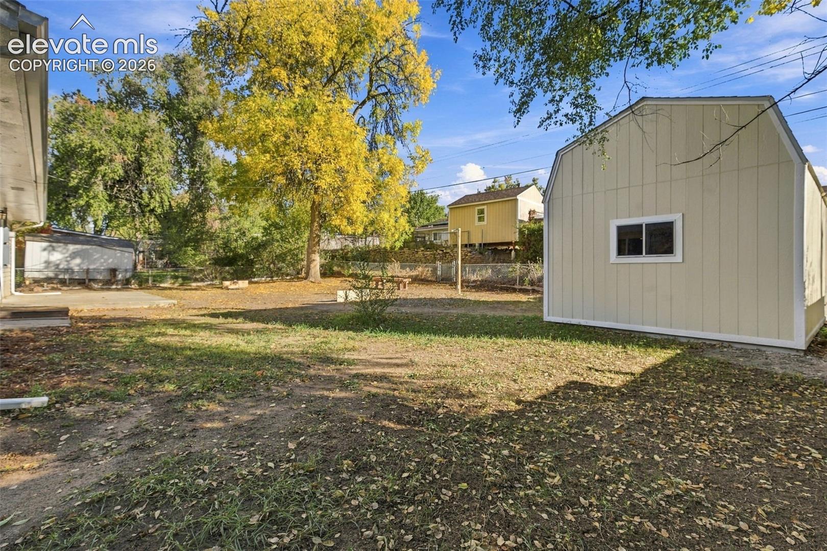 Spacious backyard featuring a detached storage shed, mature trees, concrete patio, and perimeter fencing