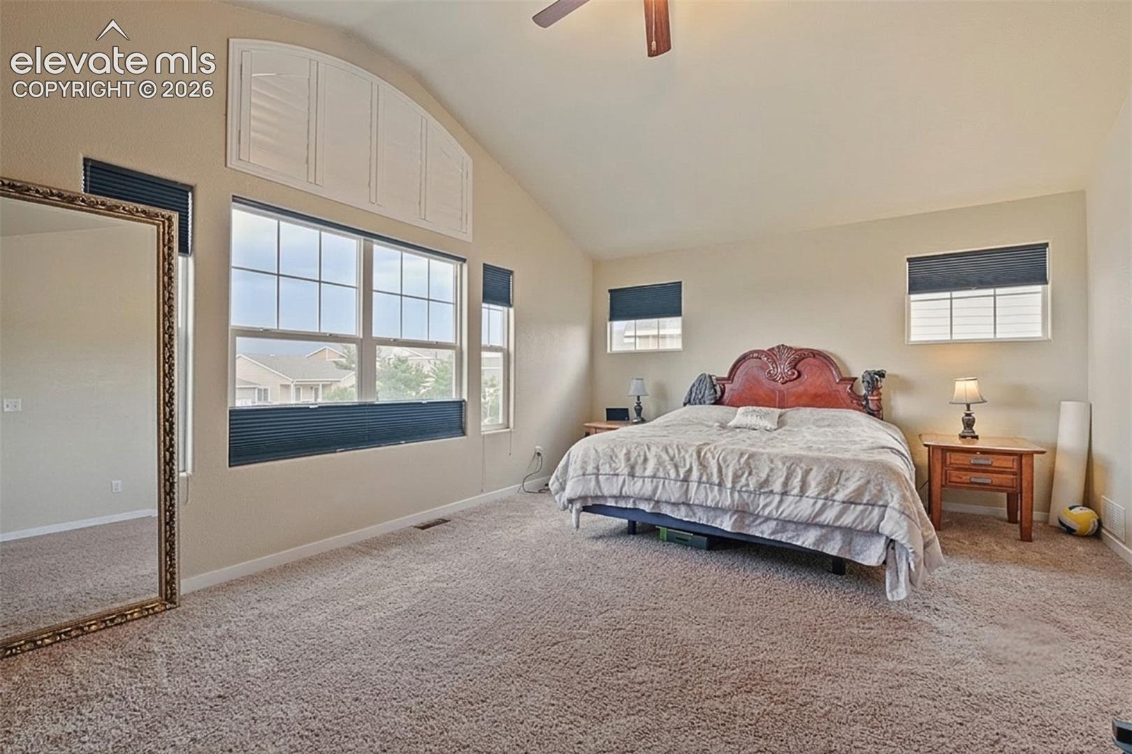 Upper Level: Bedroom featuring vaulted ceilings, a large window array with arched transom, neutral carpet, and a ceiling fan