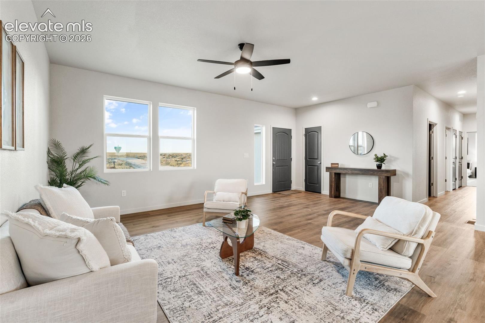 Open-concept room featuring neutral paint tones, wood-finish flooring, dual-pane windows, and a central ceiling fan with integrated lighting