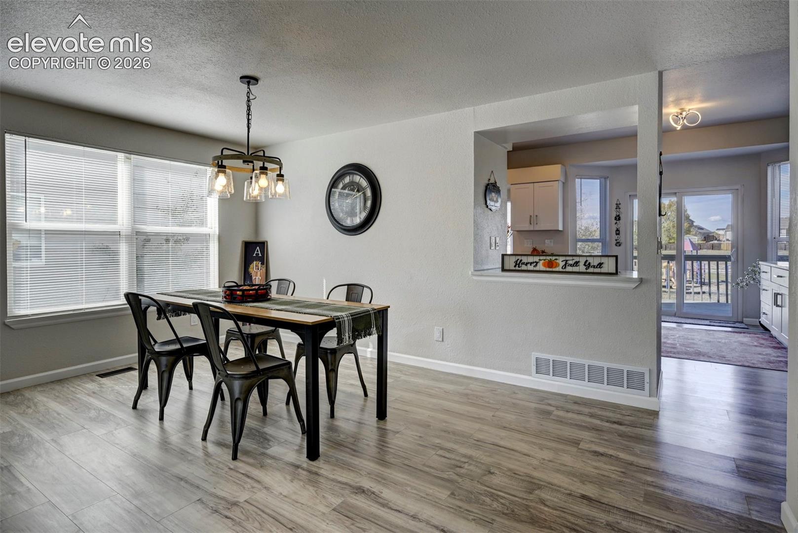 Dining area featuring wood-finish flooring, a multi-light industrial pendant fixture, and large windows with horizontal blinds
