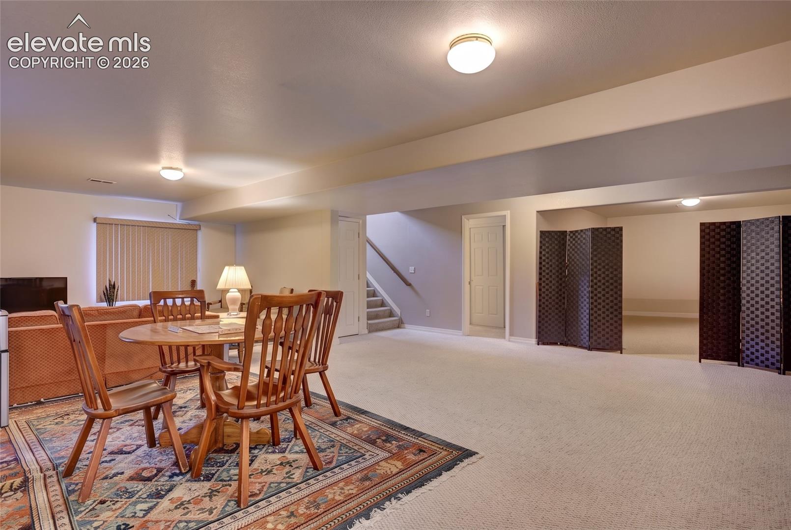 Open-concept interior space featuring neutral wall tones, wall-to-wall carpeting, recessed ceiling lighting, and a staircase with a wooden handrail