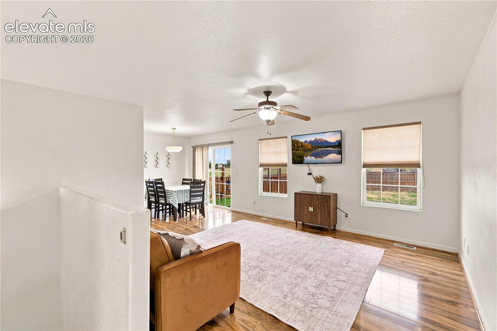 Wood-finish flooring throughout, ceiling fan with integrated lighting, multiple windows providing natural light, and sliding glass door