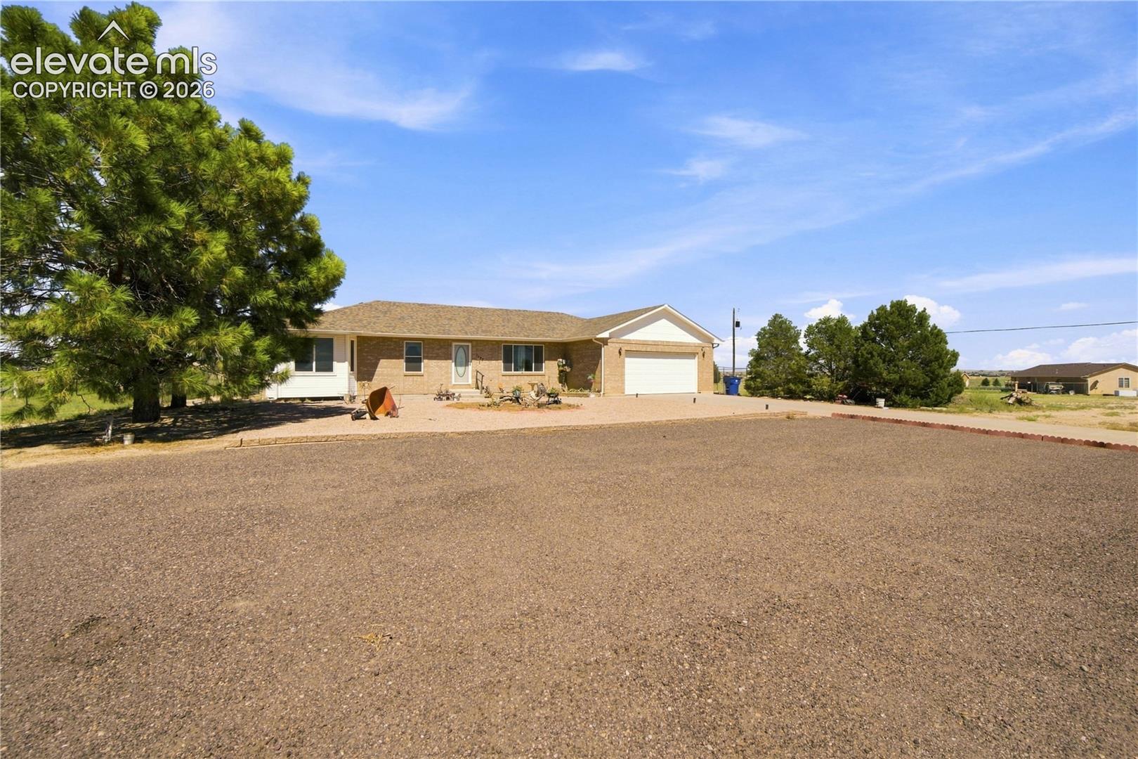 Brick exterior with an attached garage, paved driveway, and mature landscaping