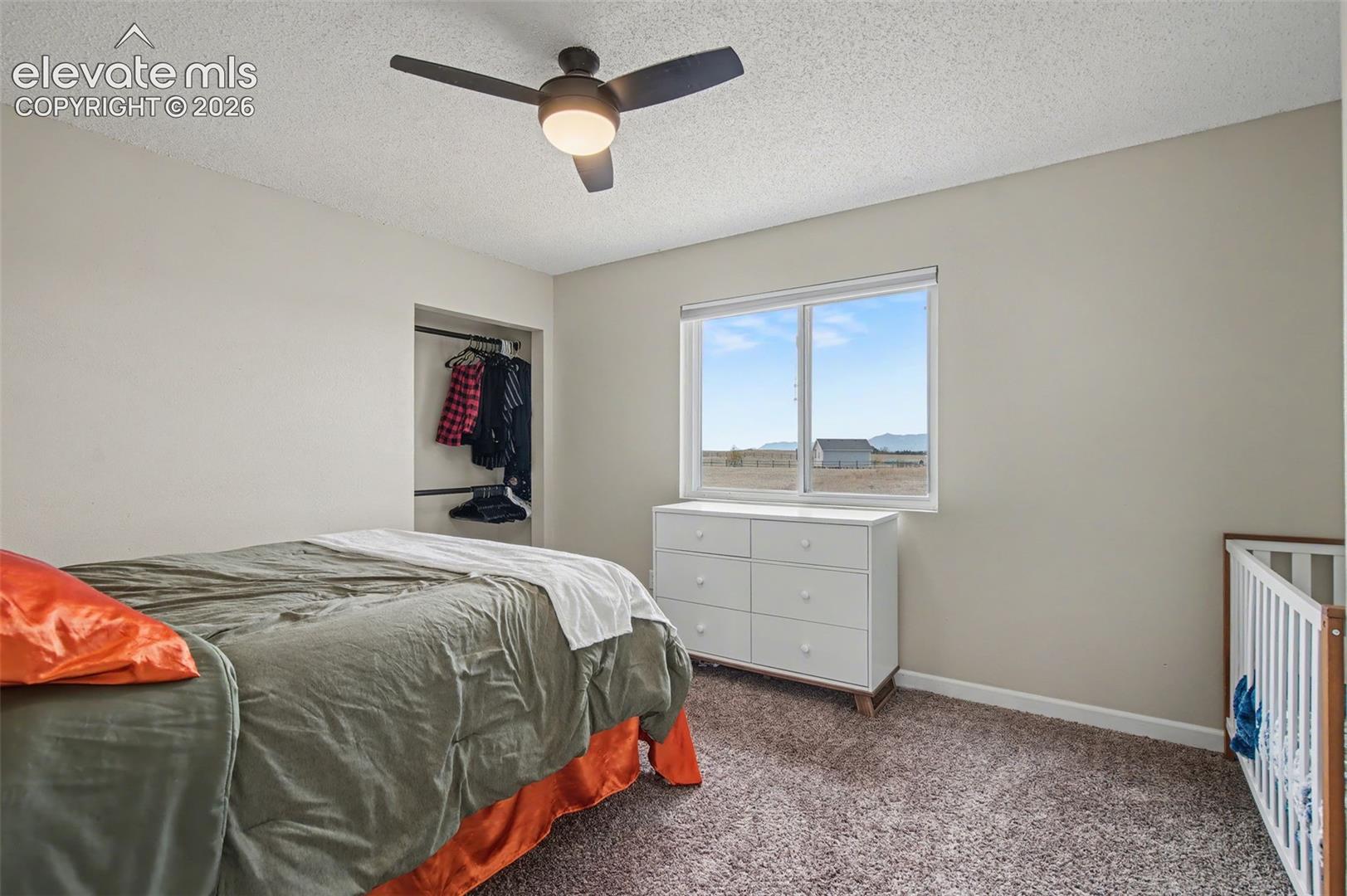 Bedroom featuring neutral wall paint, carpeted flooring, a ceiling fan with integrated lighting, a sliding window, and an open-concept built-in closet with shelving and hanging rods