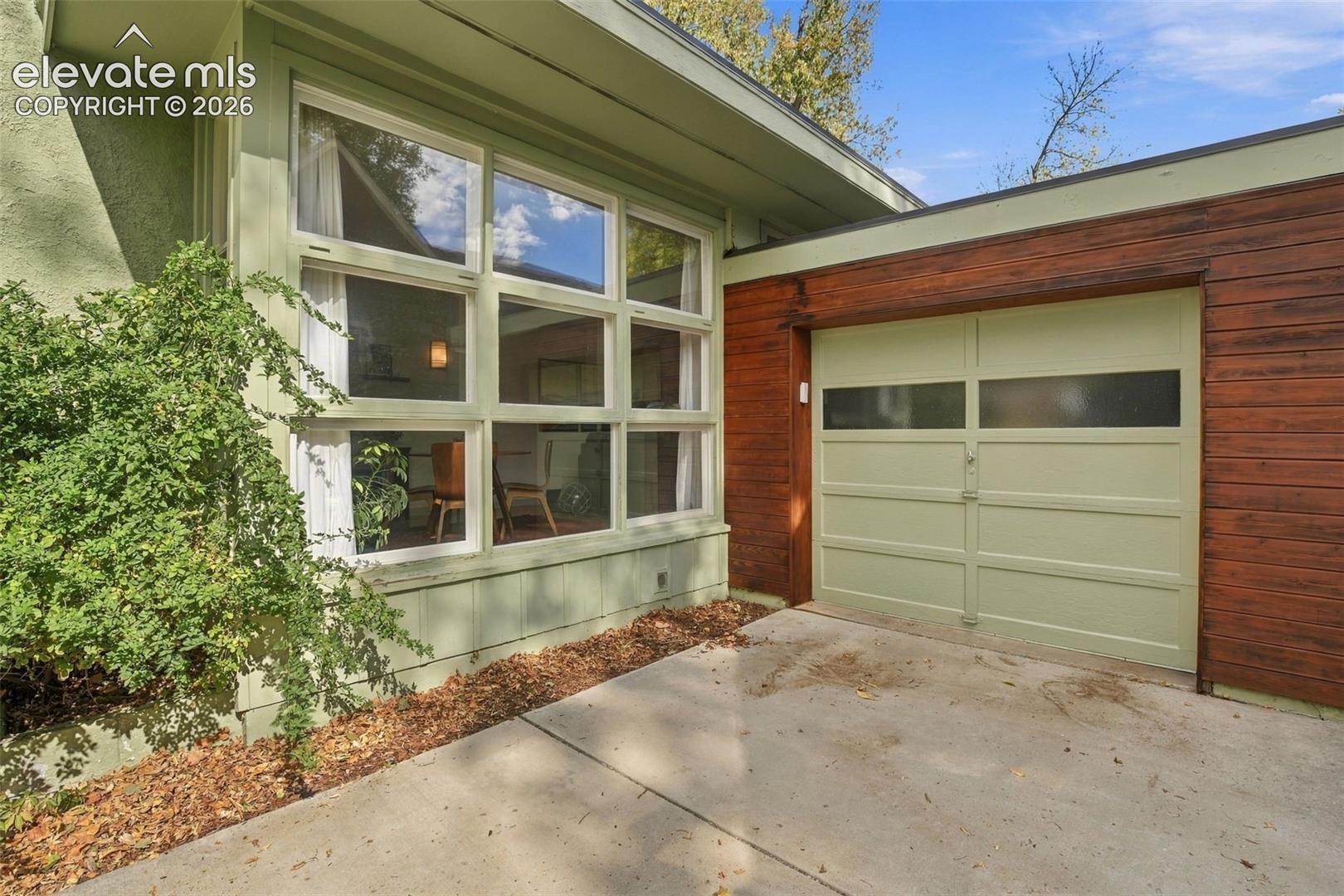 Mid-century modern exterior featuring a multi-pane grid window system, horizontal wood-plank siding, and a single-car garage with horizontal frosted glass inserts