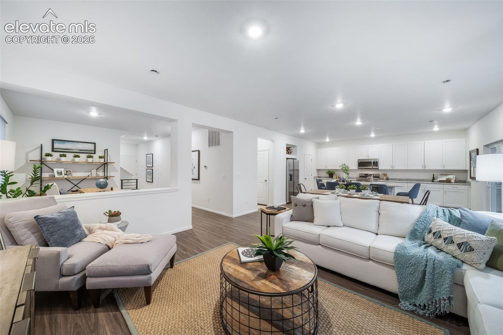 Open concept living area featuring wood-finish flooring, recessed lighting, and a kitchen with white cabinetry and stainless steel appliances
*photos of a model home*