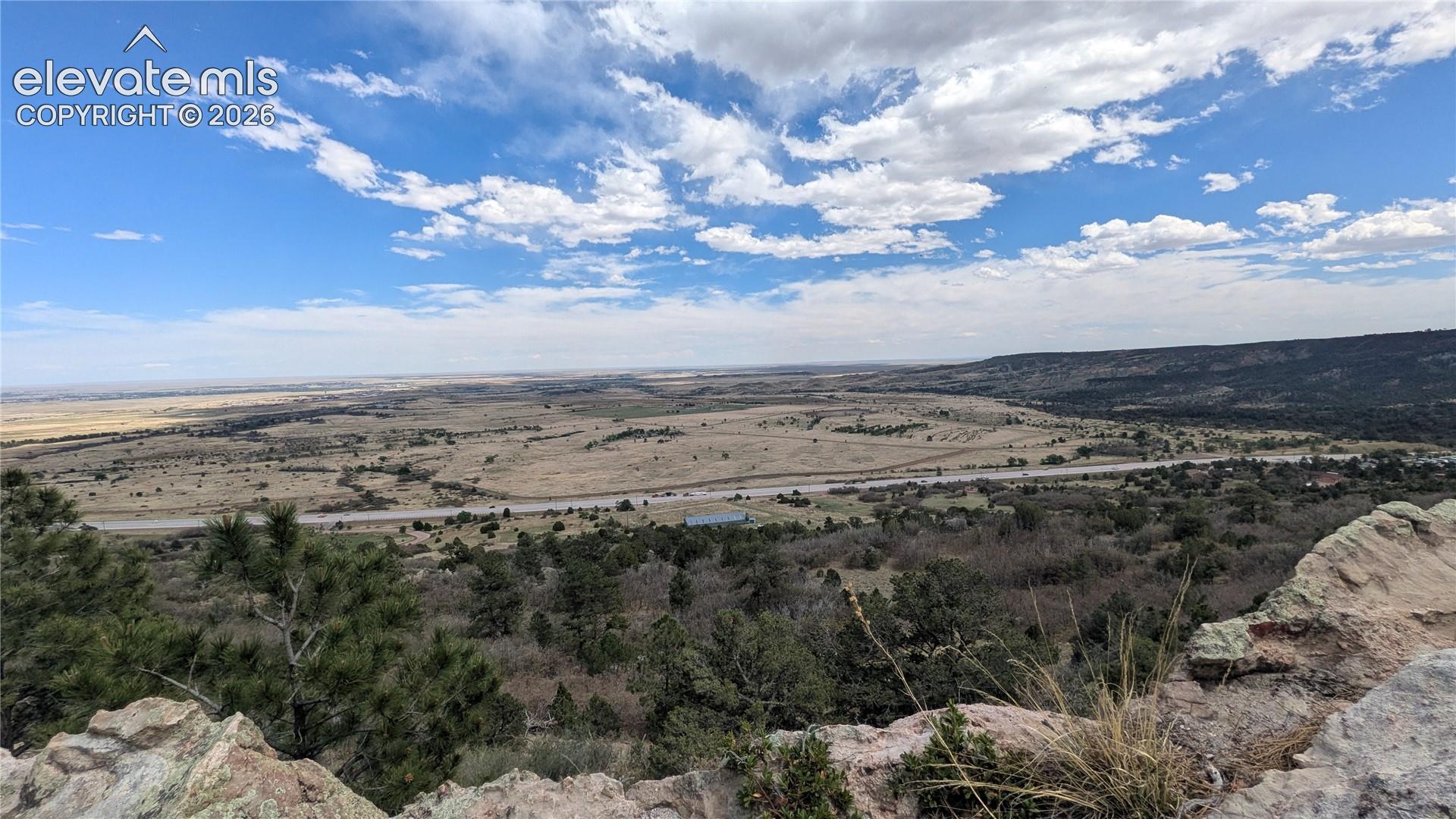 Expansive natural landscape featuring distant plains, a prominent roadway, and scattered evergreen trees