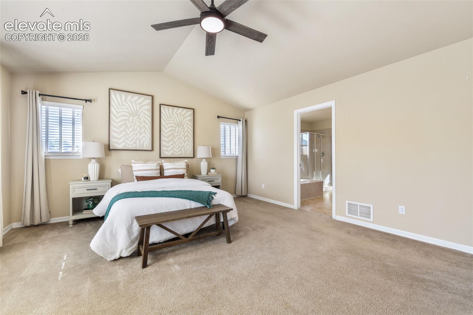 Vaulted ceiling with an attached ceiling fan, dual windows with blinds, and an open doorway leading to a bathroom featuring a bathtub and glass-enclosed shower