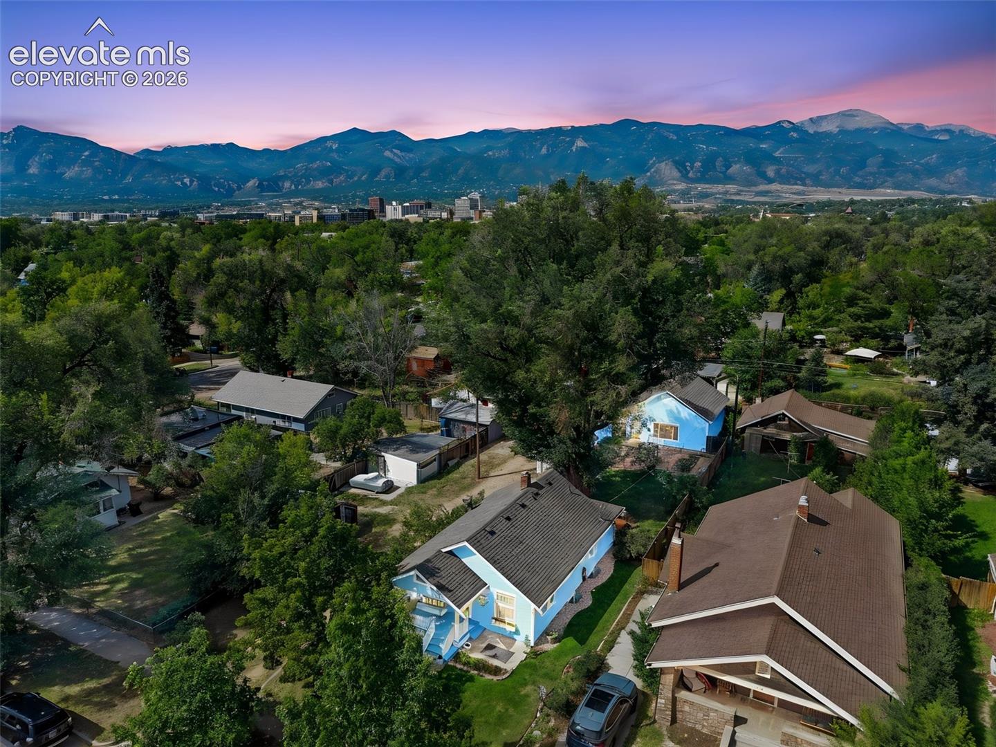 Aerial perspective featuring mountain range backdrop, mature trees, and varied residential rooflines