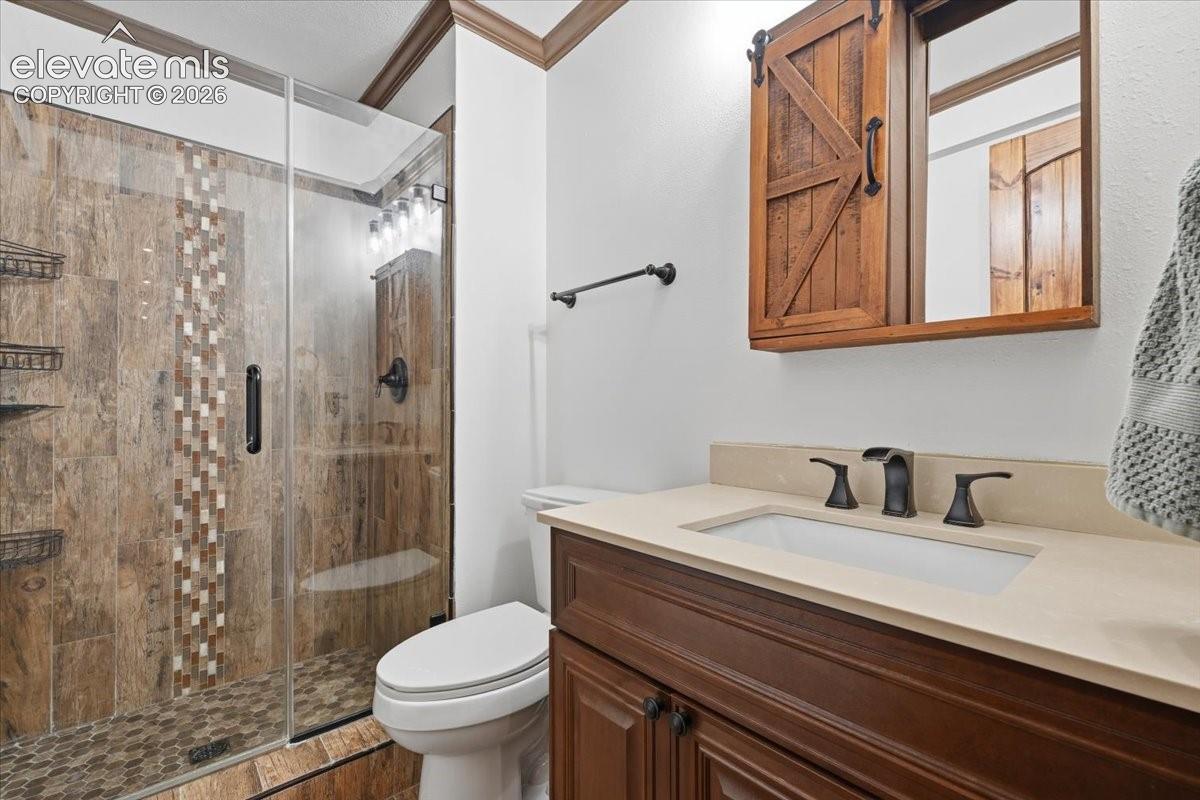 Walk-in shower with glass enclosure and mosaic tile accent, wood-finish vanity with countertop and integrated sink, barn door-style medicine cabinet, and oil-rubbed bronze fixtures