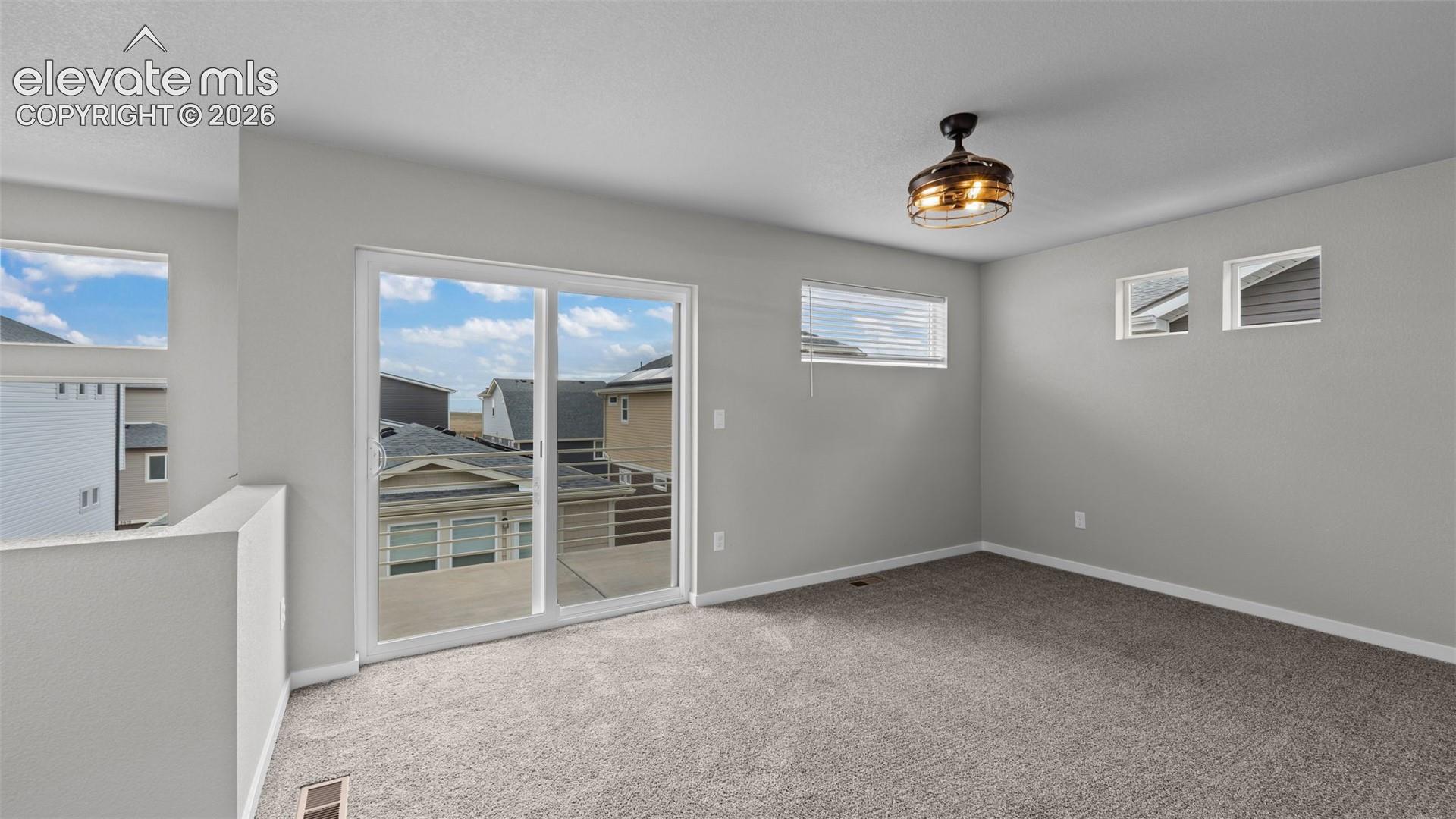 Neutral-toned interior space featuring wall-to-wall carpeting, sliding glass doors, horizontal window treatments, and a decorative industrial-style flush mount ceiling fan with integrated lighting