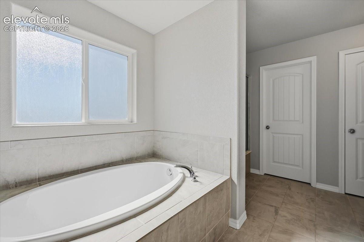 Built-in soaking tub with tile surround, obscured-glass sliding window, and ceramic tile flooring featuring two-panel interior doors
