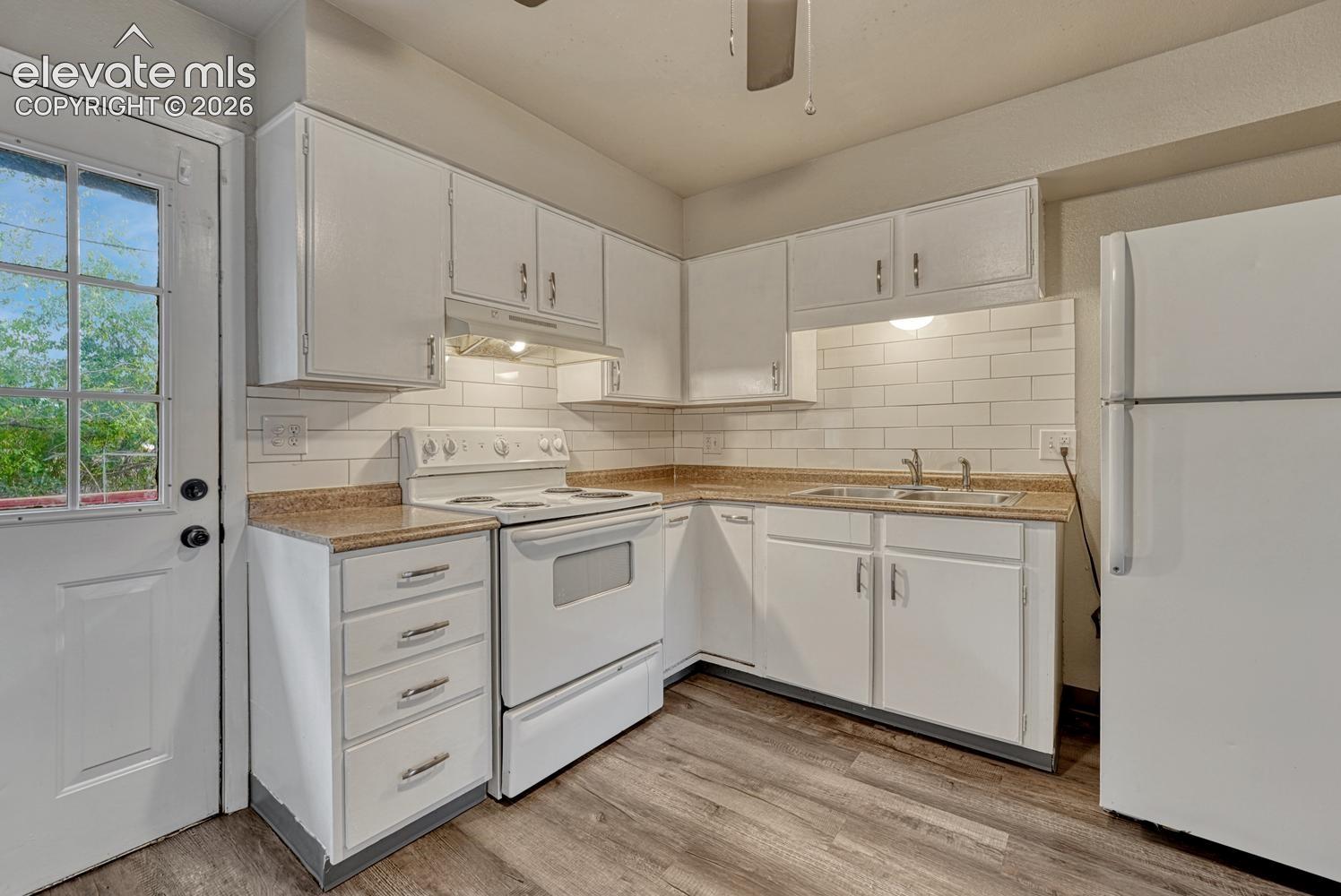White cabinetry with a subway tile backsplash, wood-finish flooring, and a glass-paneled entry door