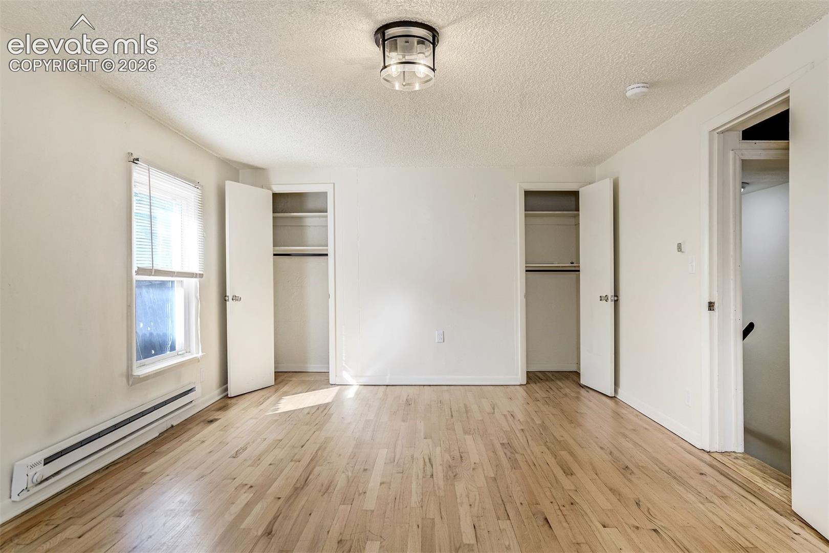 Wood-finish flooring, two reach-in closets with built-in shelving, a multi-pane window, and a flush-mount overhead light fixture