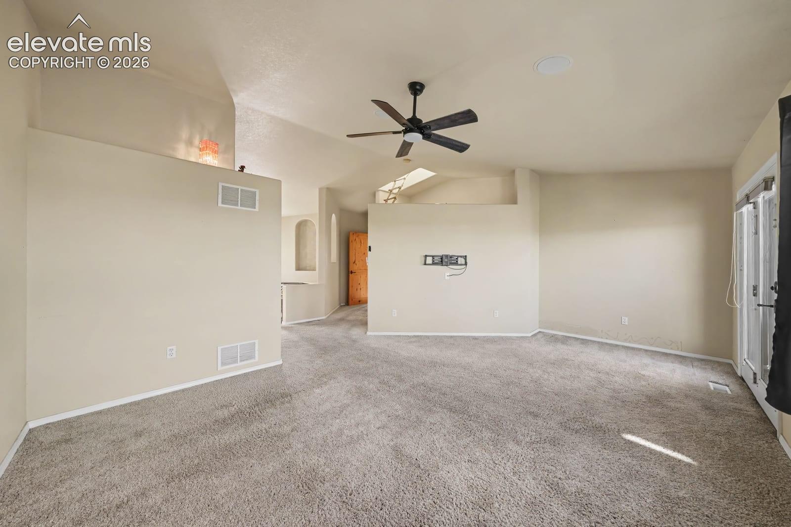 Spacious interior featuring high ceilings, neutral wall-to-wall carpeting, a ceiling fan, and large windows providing natural light