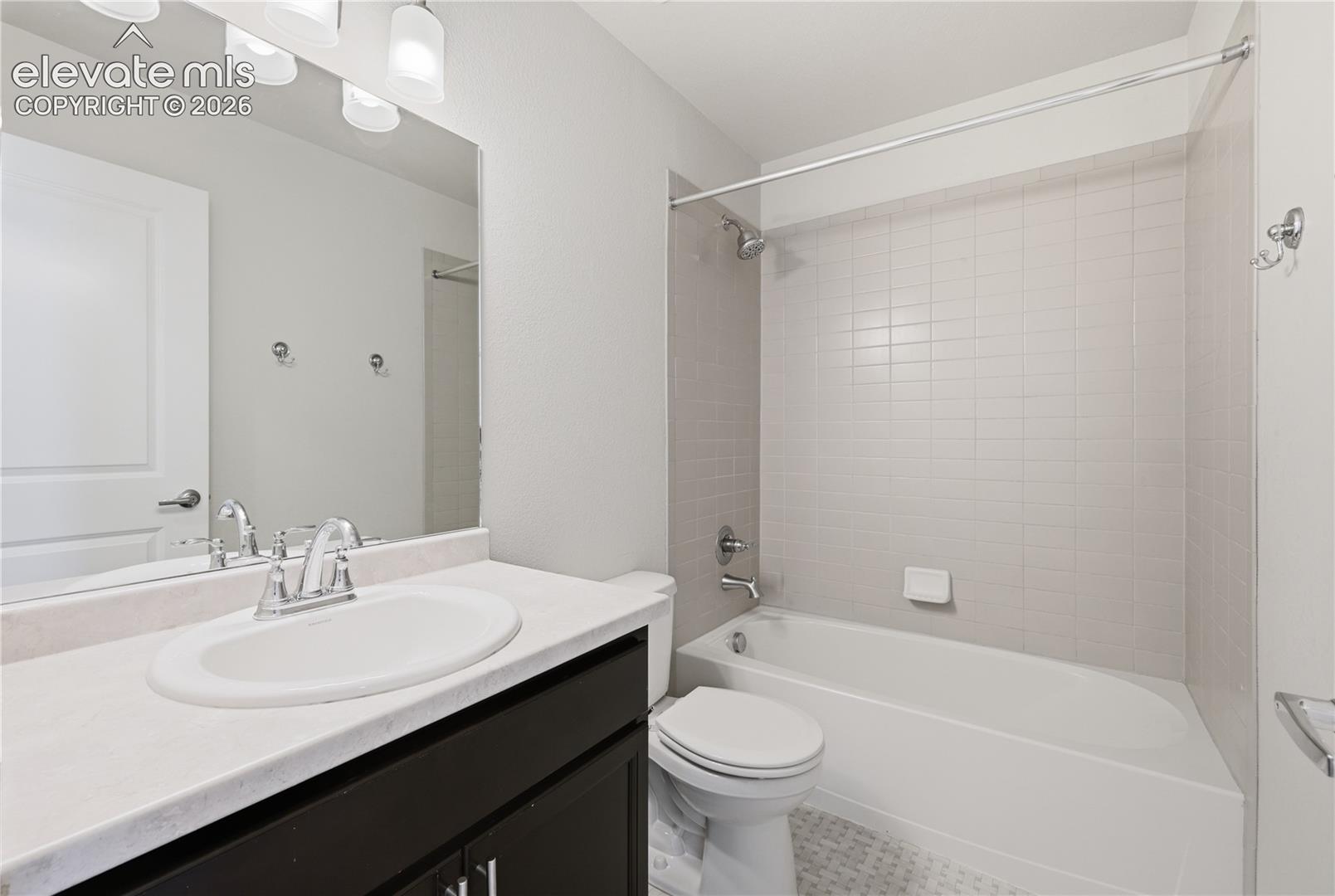 Bathroom featuring a dark wood-finish vanity with a light-colored countertop and integrated sink, chrome faucet, and expansive mirror with overhead lighting