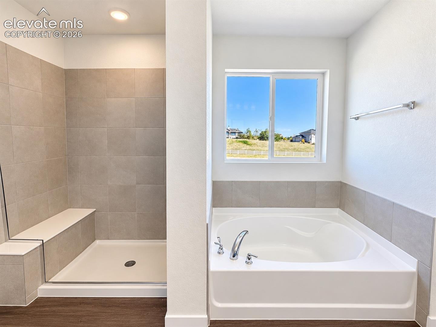 Spacious bathroom featuring a built-in soaking tub, separate walk-in shower with a tiled bench, and tile wainscoting