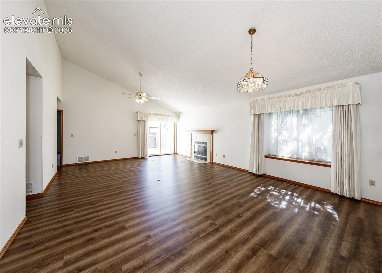 Wood-finish flooring, vaulted ceiling, built-in fireplace, ceiling fan, and sliding glass doors
