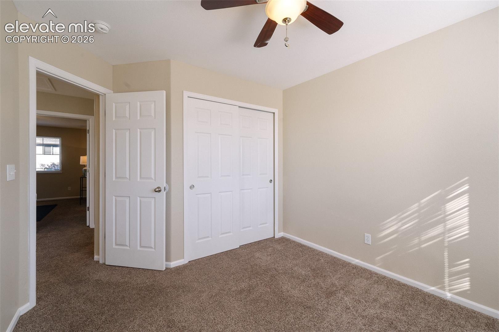 Neutral-toned interior space featuring carpeting, a ceiling fan with integrated light, a six-panel passage door, and a sliding-door closet