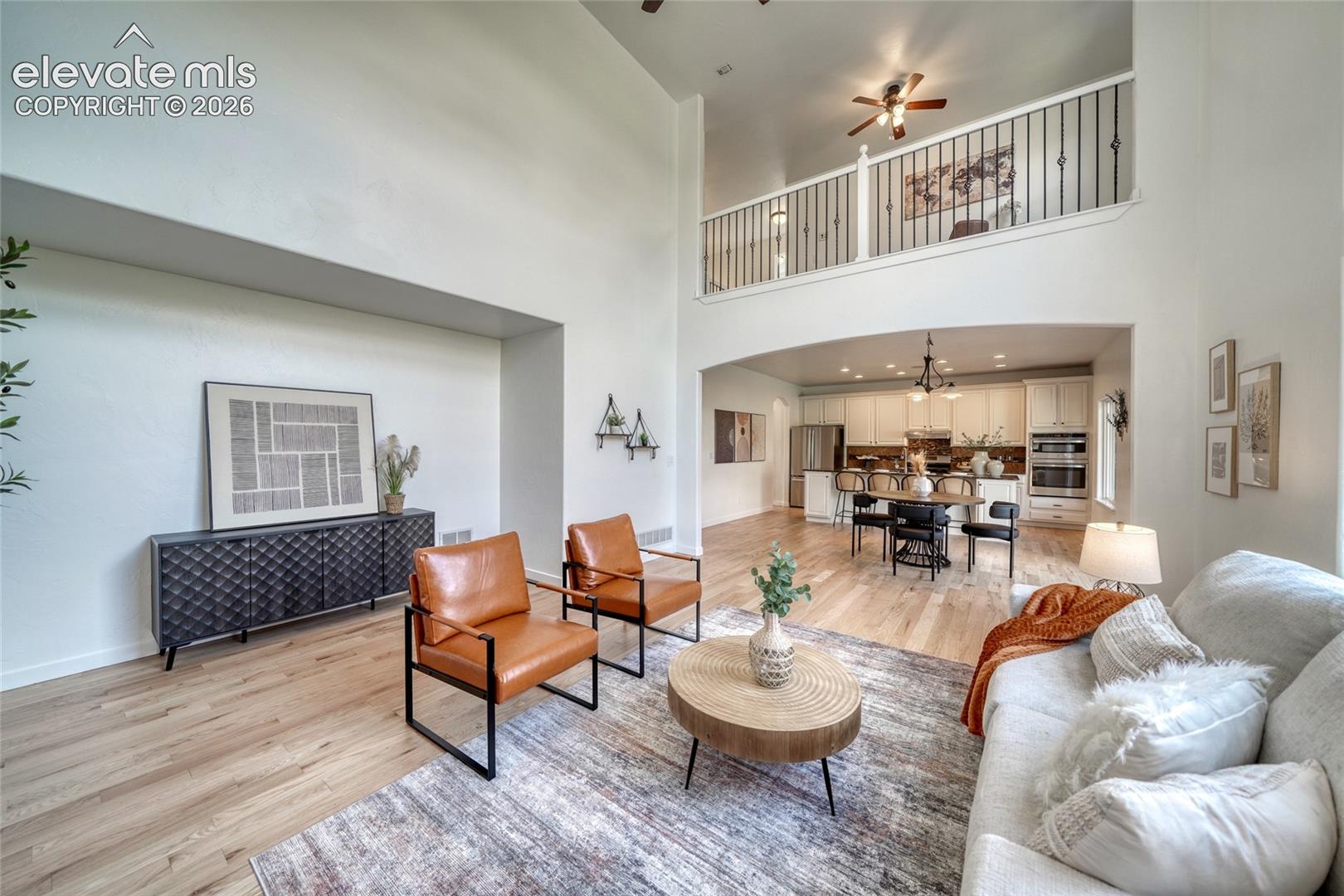 Vaulted ceiling with an open loft, light wood-finish flooring, and a kitchen with white cabinetry and stainless steel appliances