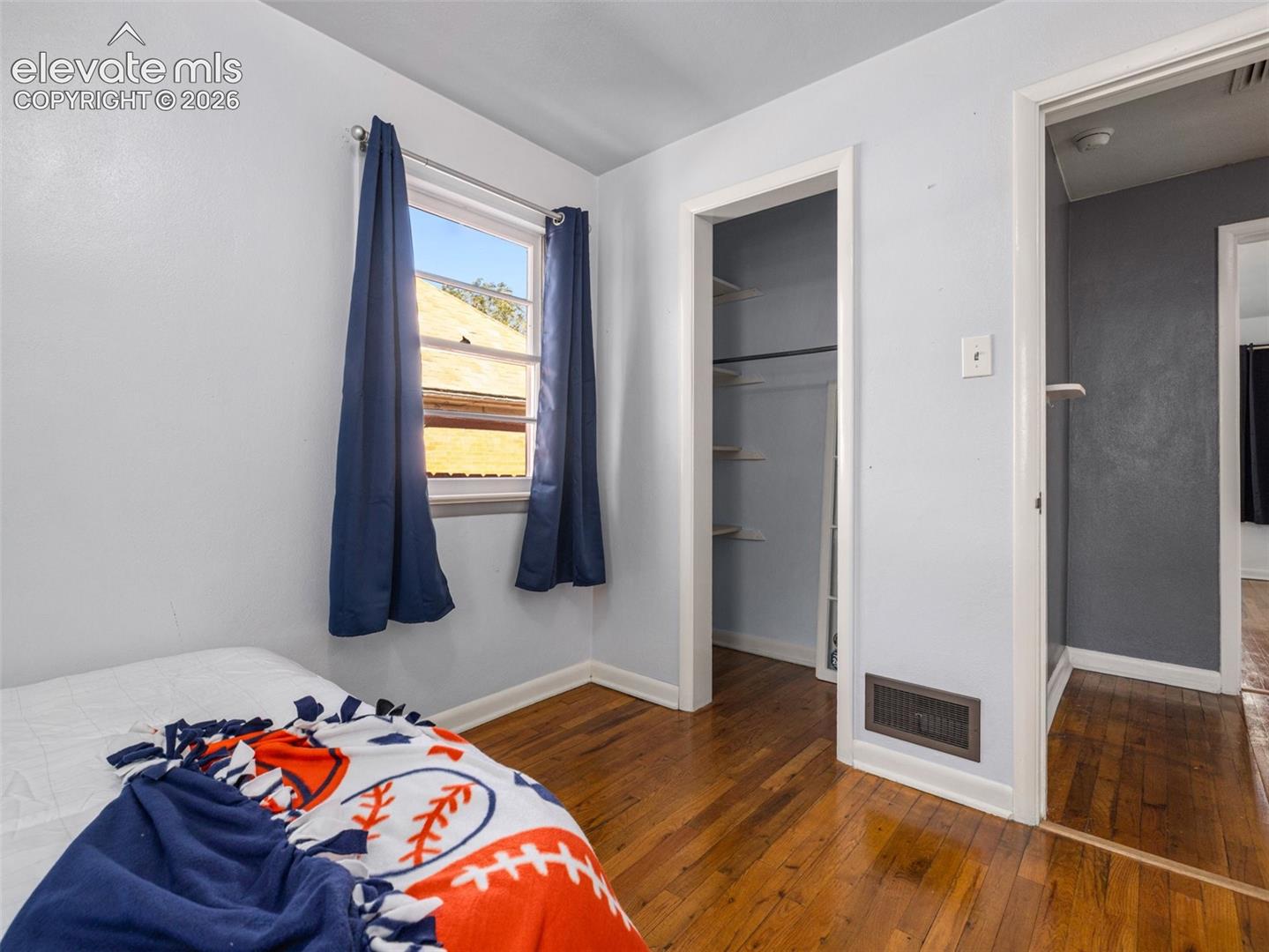 Room featuring wood-finish flooring, a single window, and a built-in closet with shelving