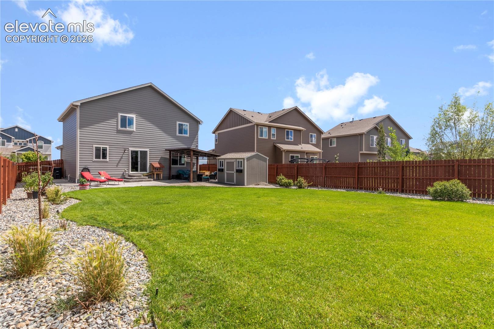 Expansive backyard featuring a manicured lawn, established landscaping, and a privacy fence