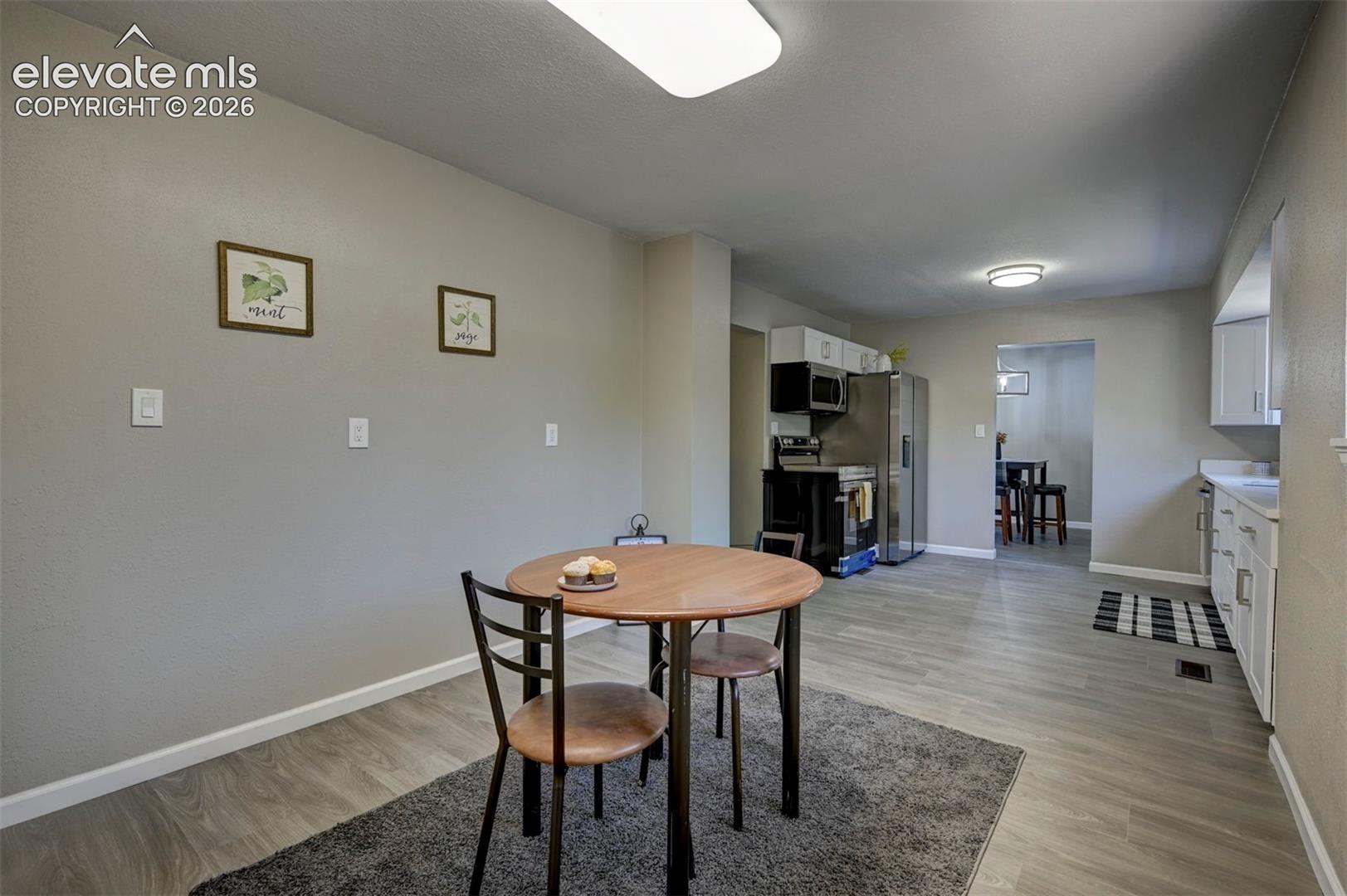 Open-concept space featuring wood-finish flooring, white cabinetry, built-in stainless steel appliances, and flush-mount ceiling lighting