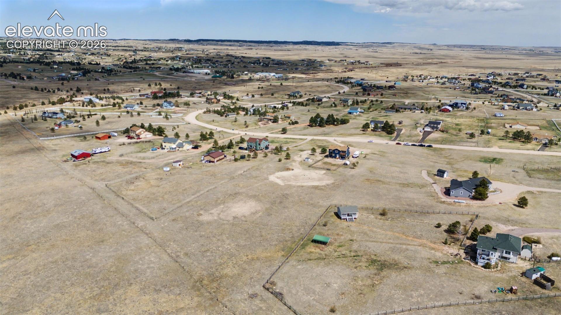 Aerial perspective of a sprawling rural lot featuring native grasslands, perimeter fencing, and open horizon topography
