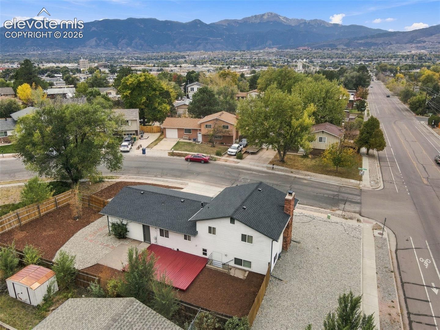 White exterior siding, dark-toned asphalt shingle roof, red-finished patio cover, exterior brick chimney, and prominent mountain backdrop