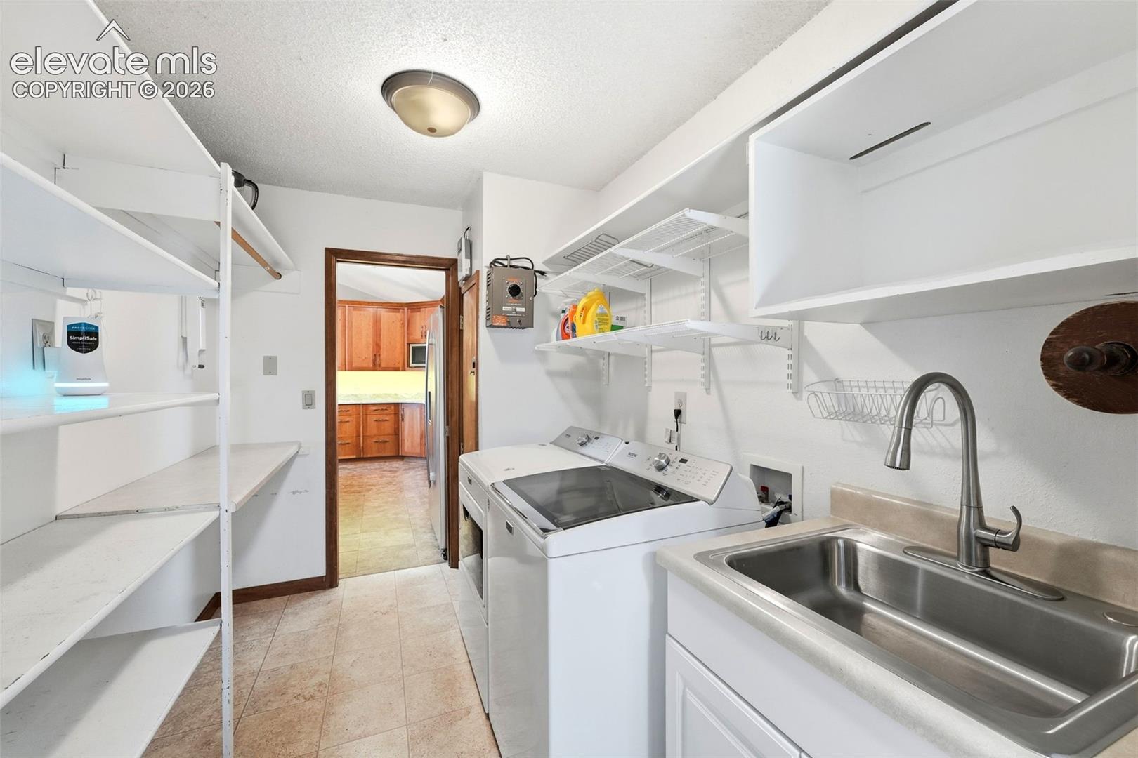 Laundry room featuring a utility sink, white cabinetry, built-in shelving, and tile flooring
