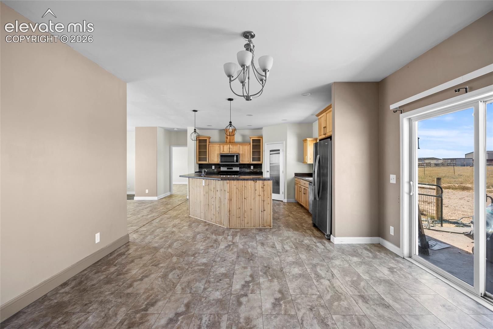 Kitchen featuring wood-finish cabinetry, a large central island with vertical wood-plank siding, stone-surface countertops, tile flooring, and sliding glass exterior doors