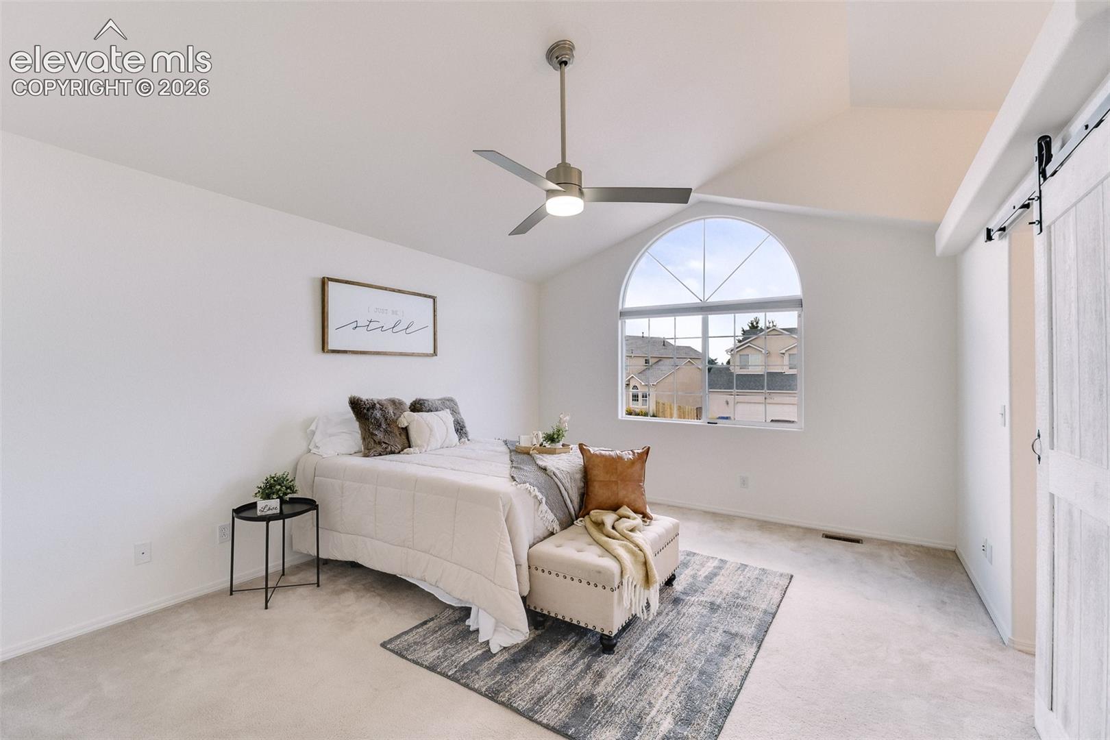 Vaulted ceiling, arched window, ceiling fan with integrated lighting, and a white barn door