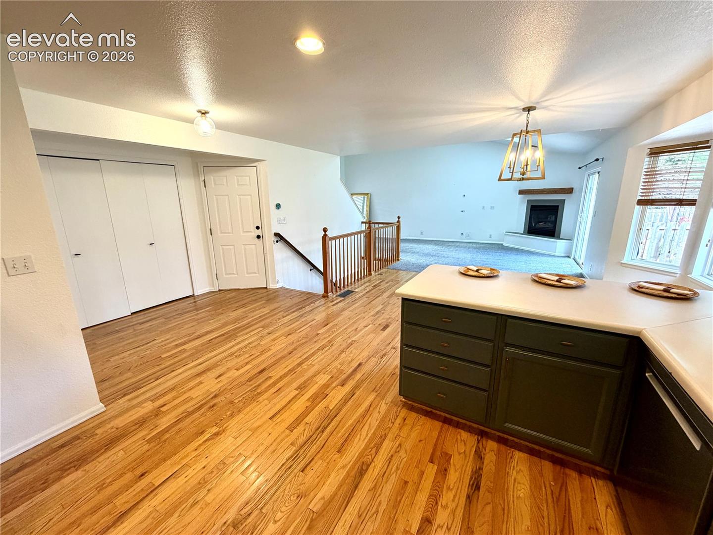 Open-concept living space featuring wood-finish flooring, extensive counter space with dark green cabinetry, a living area with a fireplace, and a wood railing staircase