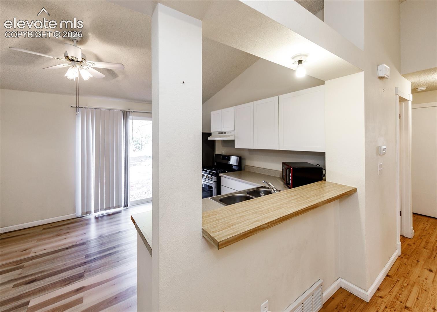 Kitchen featuring white cabinetry, a wood-finish countertop, dual-basin stainless steel sink, and wood-finish flooring