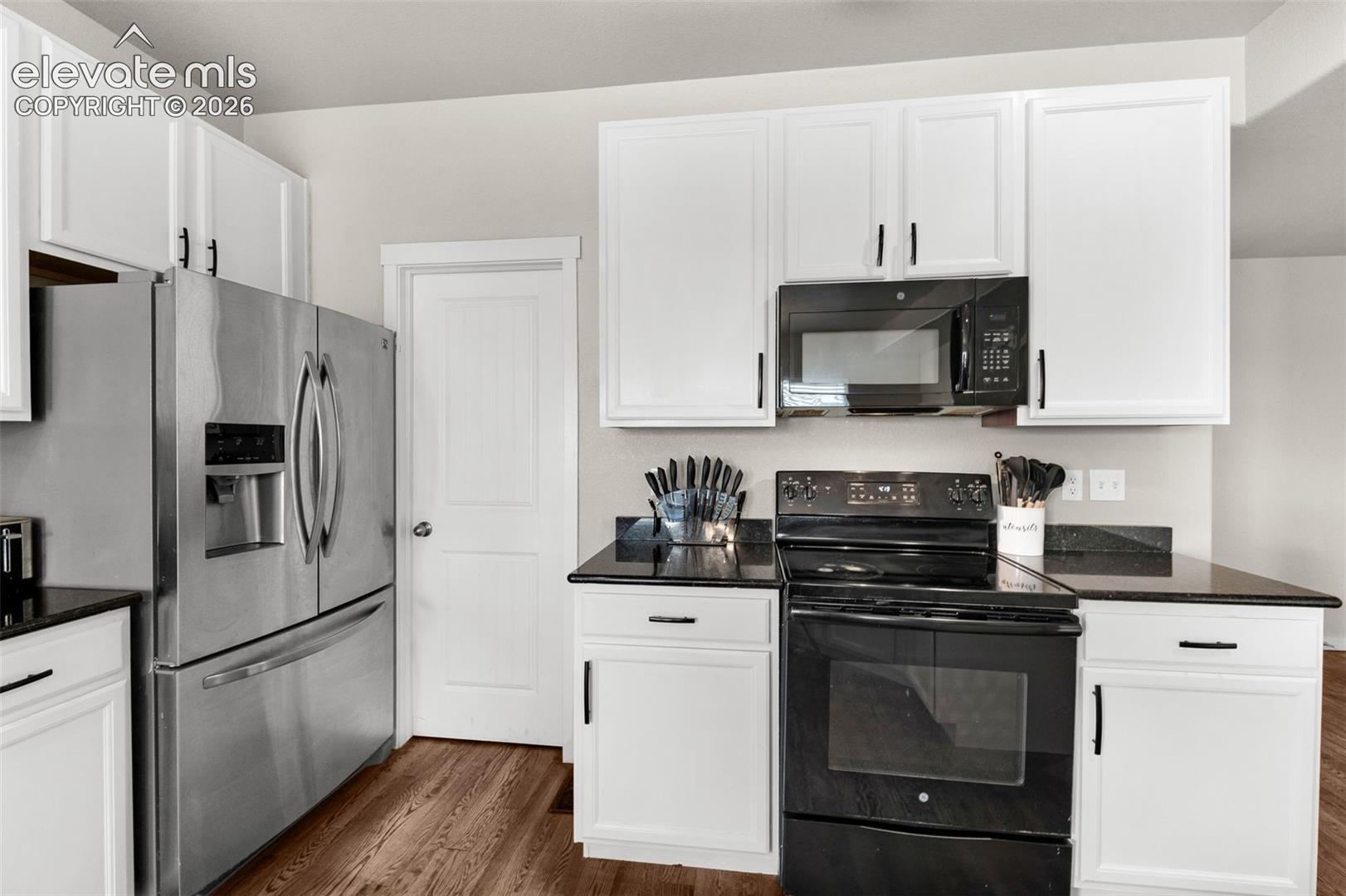 Kitchen featuring white cabinetry with black hardware, dark stone-finish countertops, stainless steel refrigerator, and wood-finish flooring
