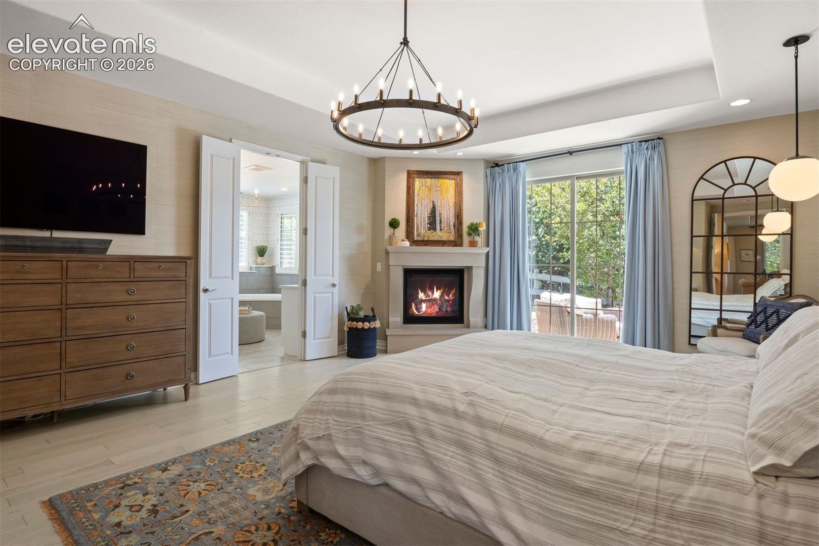 Recessed ceiling with a contemporary chandelier, corner fireplace with a stone surround, sliding glass doors, and wood-finish flooring