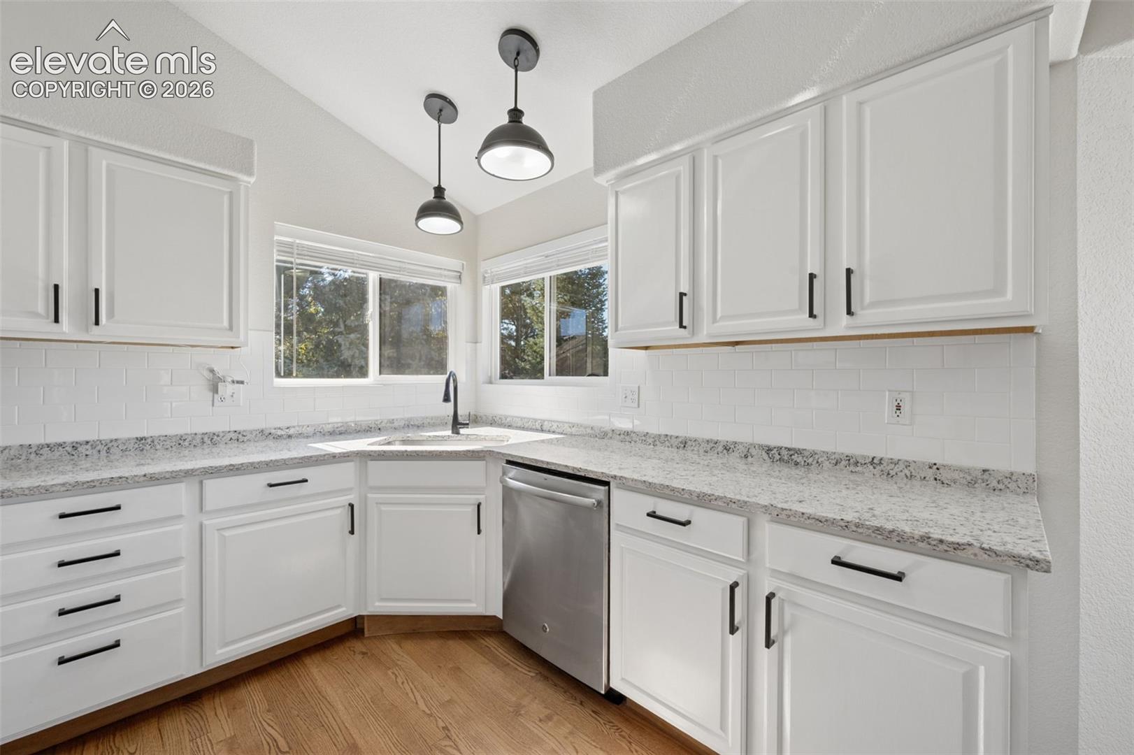 Kitchen featuring white cabinetry with matte black hardware, speckled stone-finish countertops, white subway tile backsplash, stainless steel dishwasher, and two pendant lights