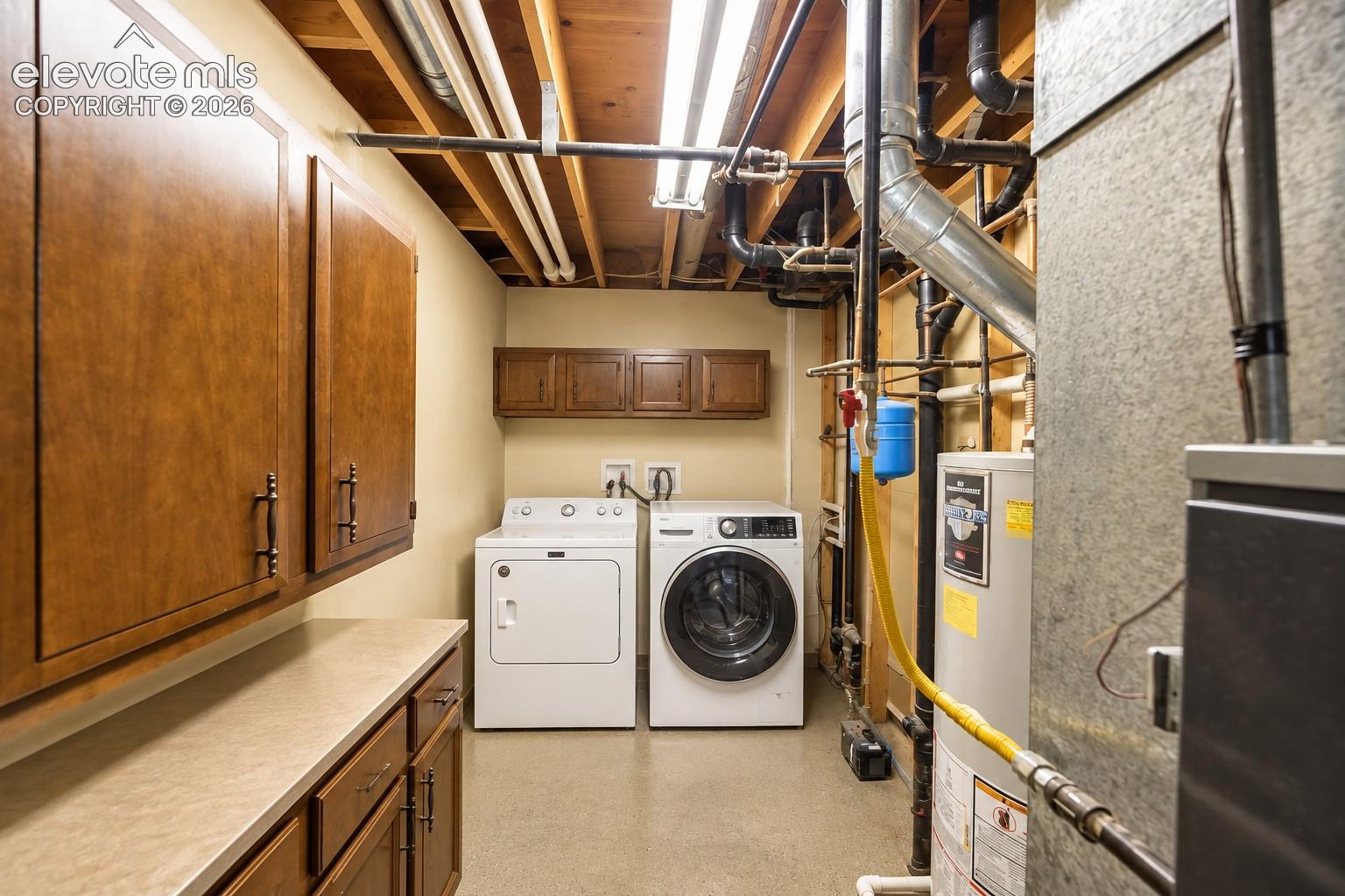 Utility room featuring built-in wood cabinetry, a light-toned countertop, exposed ceiling joists, and a water heater