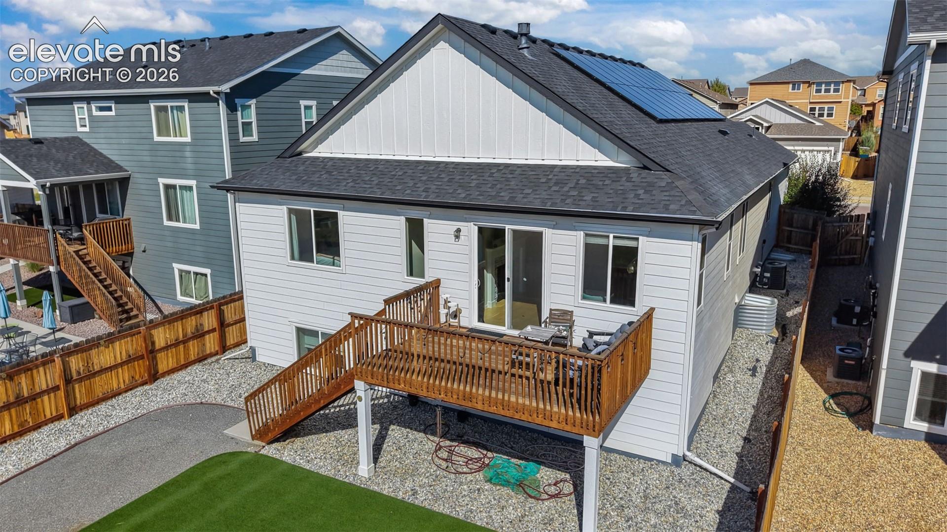 Raised wood deck, solar panels, gravel landscaping, horizontal siding, and a fenced perimeter