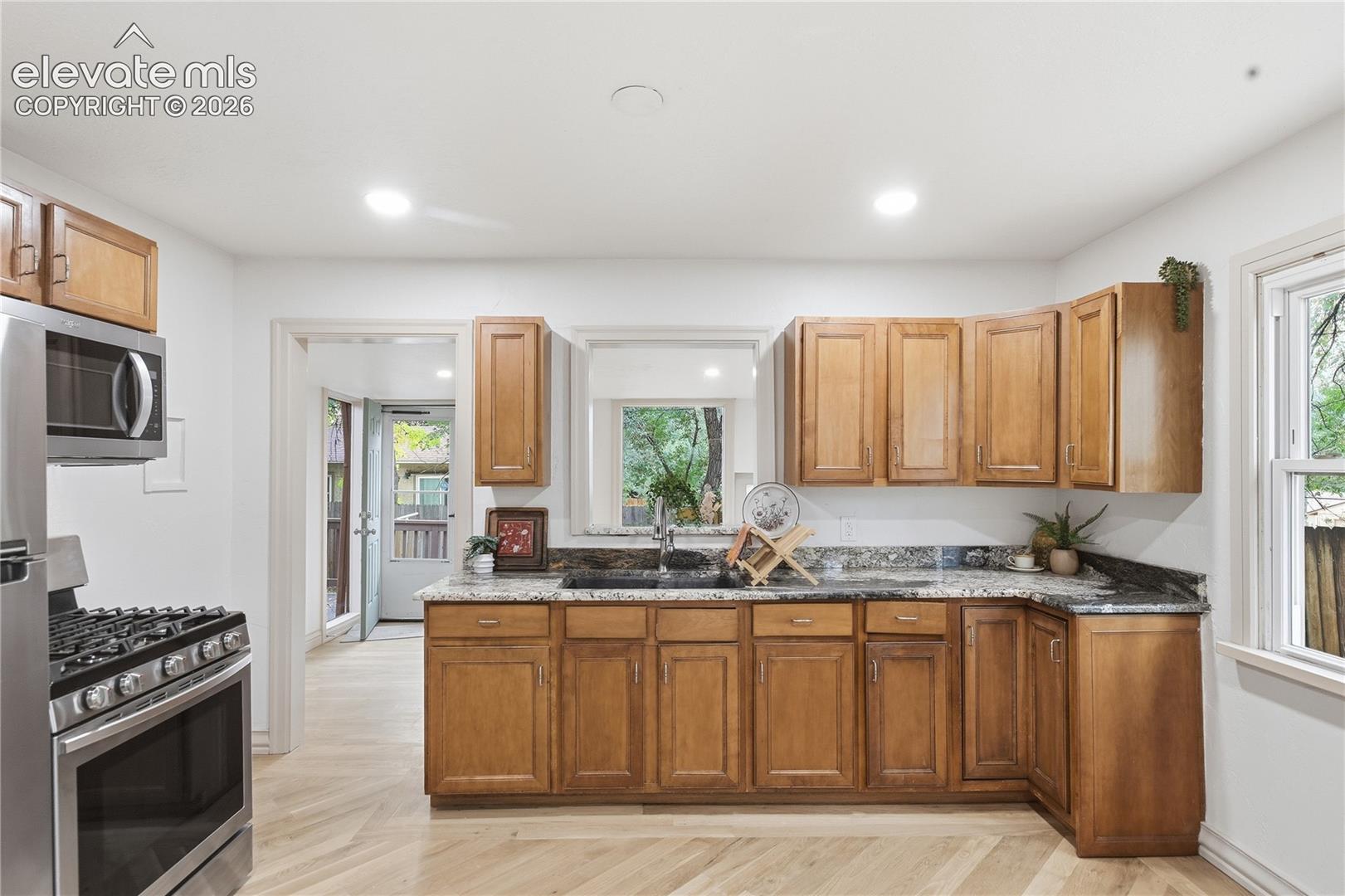 Kitchen featuring natural wood cabinetry, stone-finish countertops, stainless steel range with overhead microwave, and herringbone-pattern wood-finish flooring