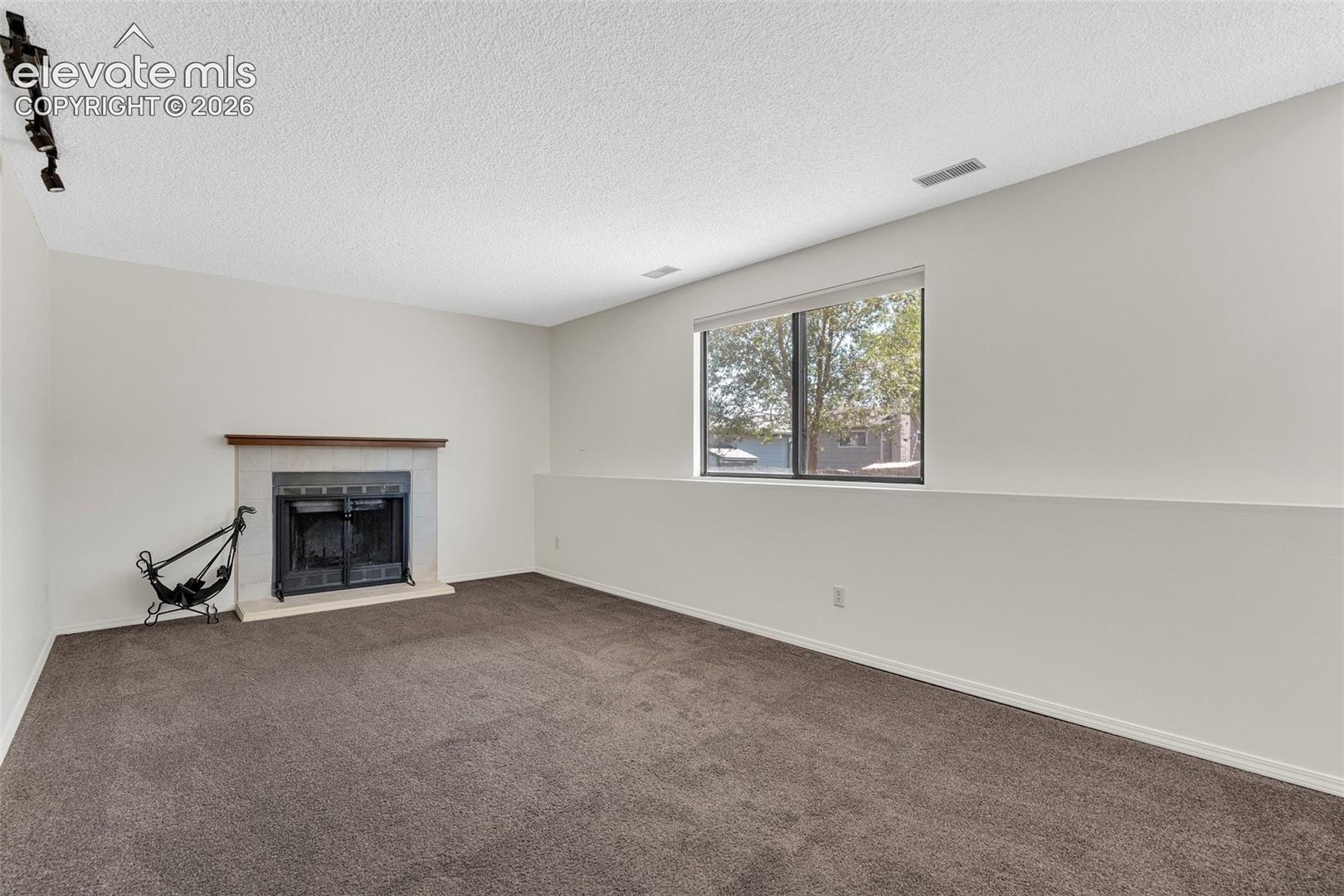 Wood fireplace with a wood mantle, carpet flooring, and a large window