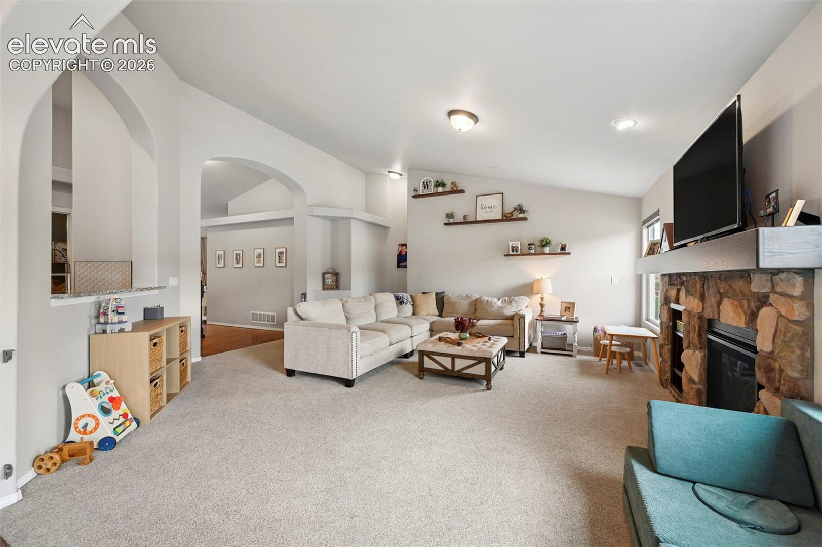 Living area featuring vaulted ceilings, stone-faced fireplace with a wood mantel, arched wall openings, and recessed lighting
