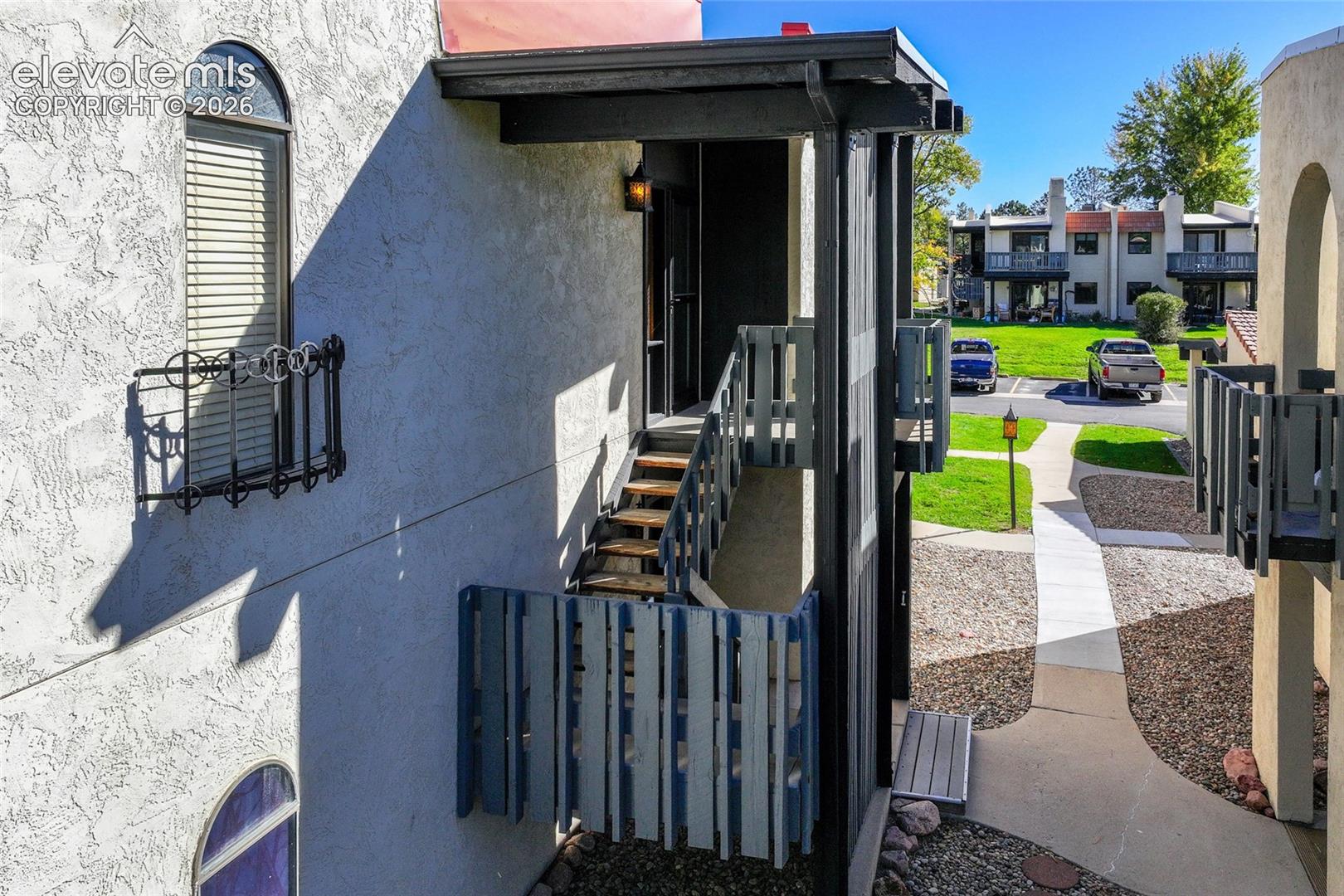 Stucco exterior featuring arched windows, decorative wrought-iron window guards, and a covered exterior staircase with vertical-slat railings